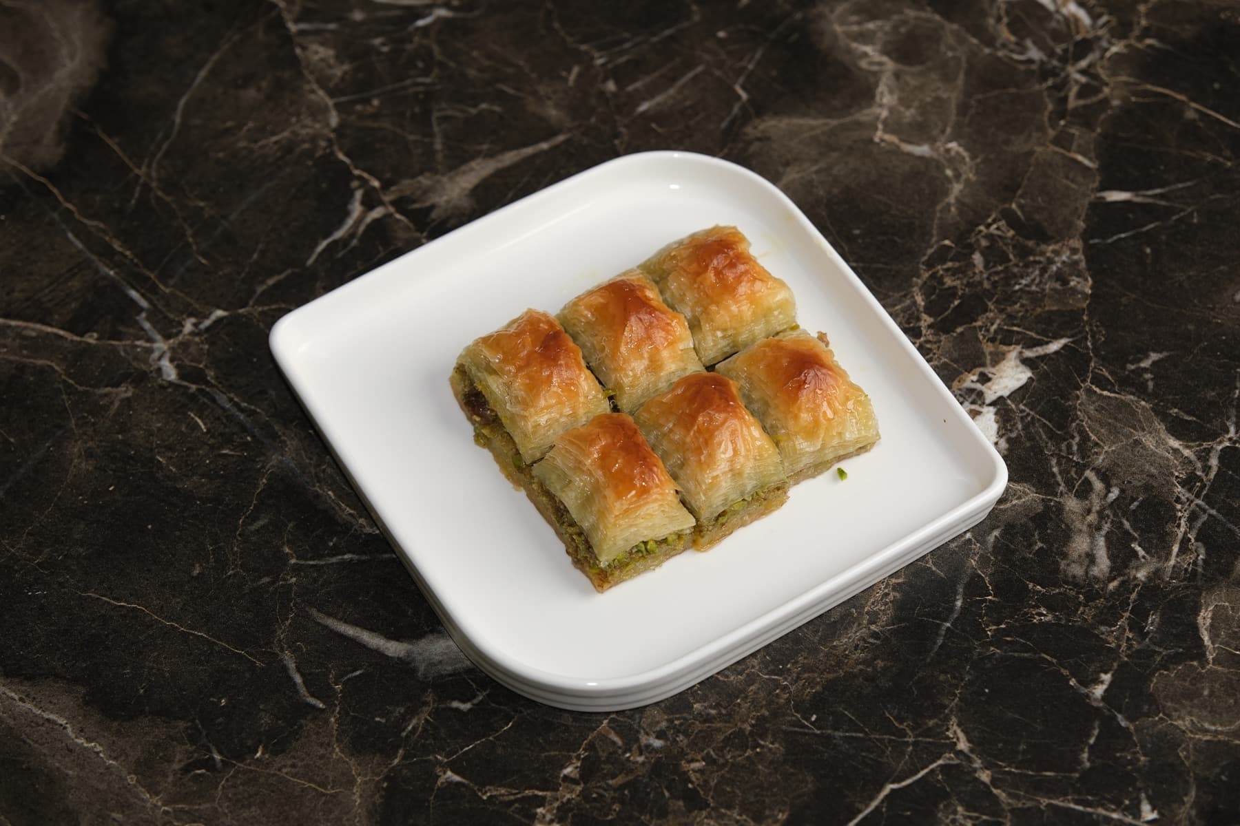 Beyaz tabakta fıstıklı baklava porsiyonu